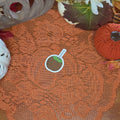 A sticker in the shape of a caramel apple sitting on an orange doily with autumn decor in the background.