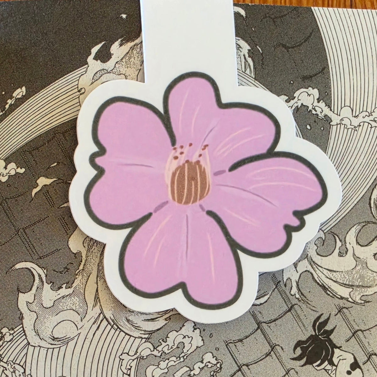 A magnetic bookmark featuring a stylized pink cherry blossom (sakura) flower with a brown center and black outline, shown on top of a Japanese wave manga print background.