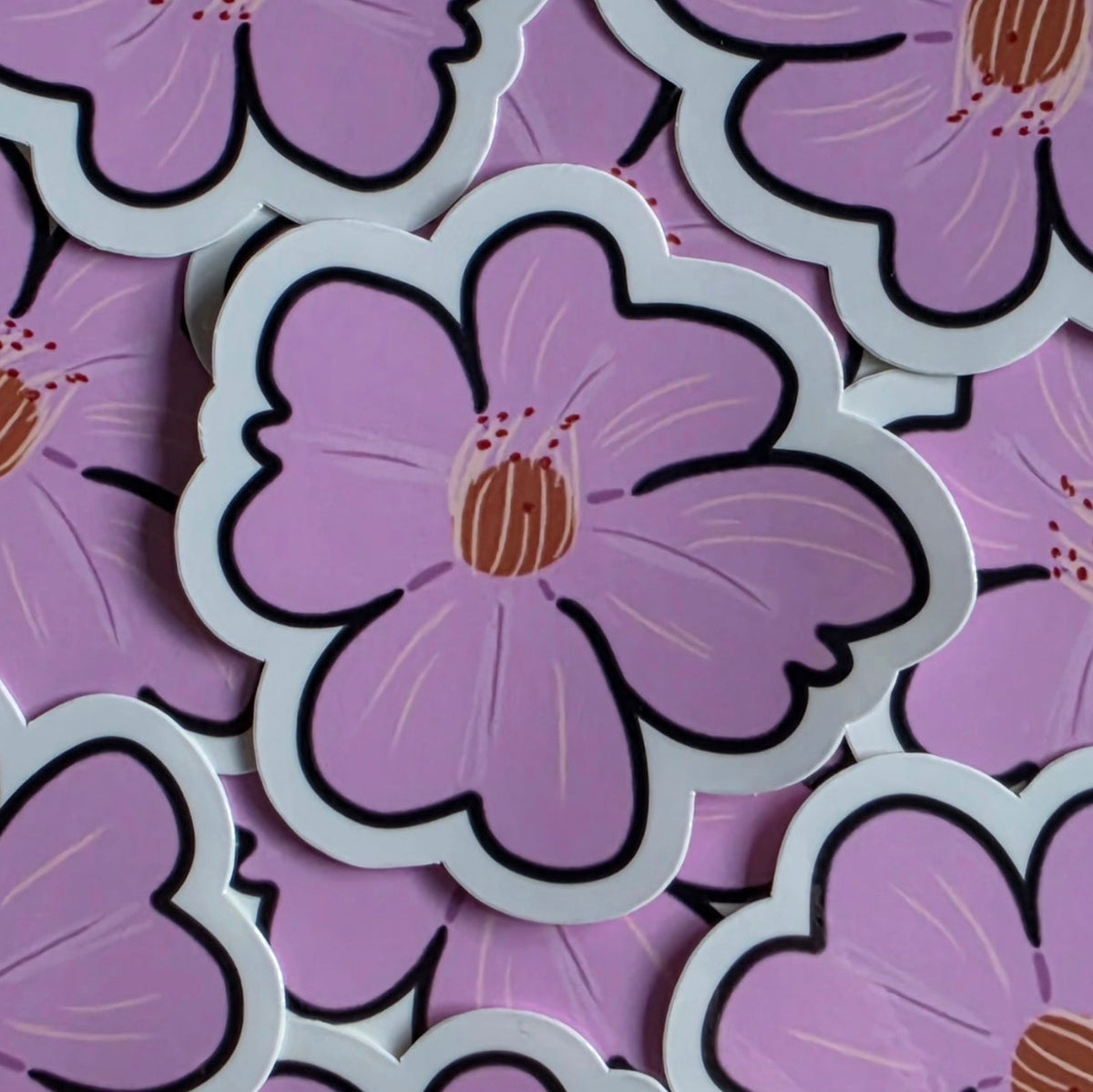A close-up of die-cut sakura (cherry blossom) flower stickers with pink petals, black outlines, and tan centers, layered on top of similar flowers.