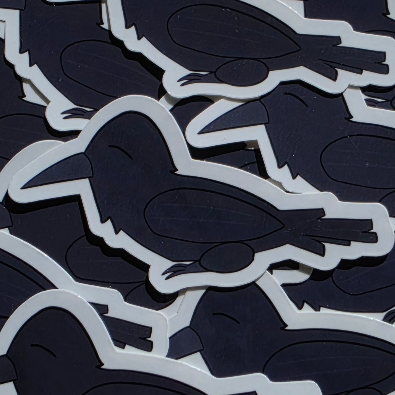 A close-up pile of crow or raven stickers with a black body and white outline, layered over one another.