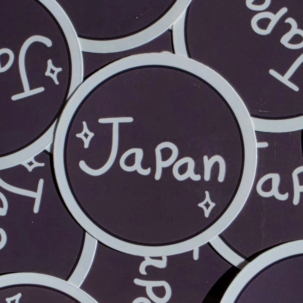 A close-up of round brown stickers with a white border and the word 'Japan' written in white script, surrounded by matching stickers.