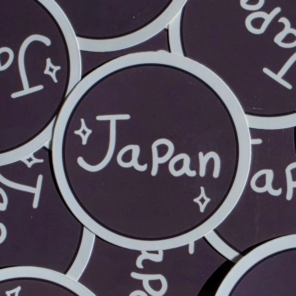 A close-up of round brown stickers with a white border and the word 'Japan' written in white script, surrounded by matching stickers.