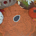 A sticker in the shape of a pinecone sitting on an orange doily with autumn decor in the background.