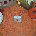 A sticker in the shape of a pumpkin spice candle sitting on an orange doily with autumn decor in the background.