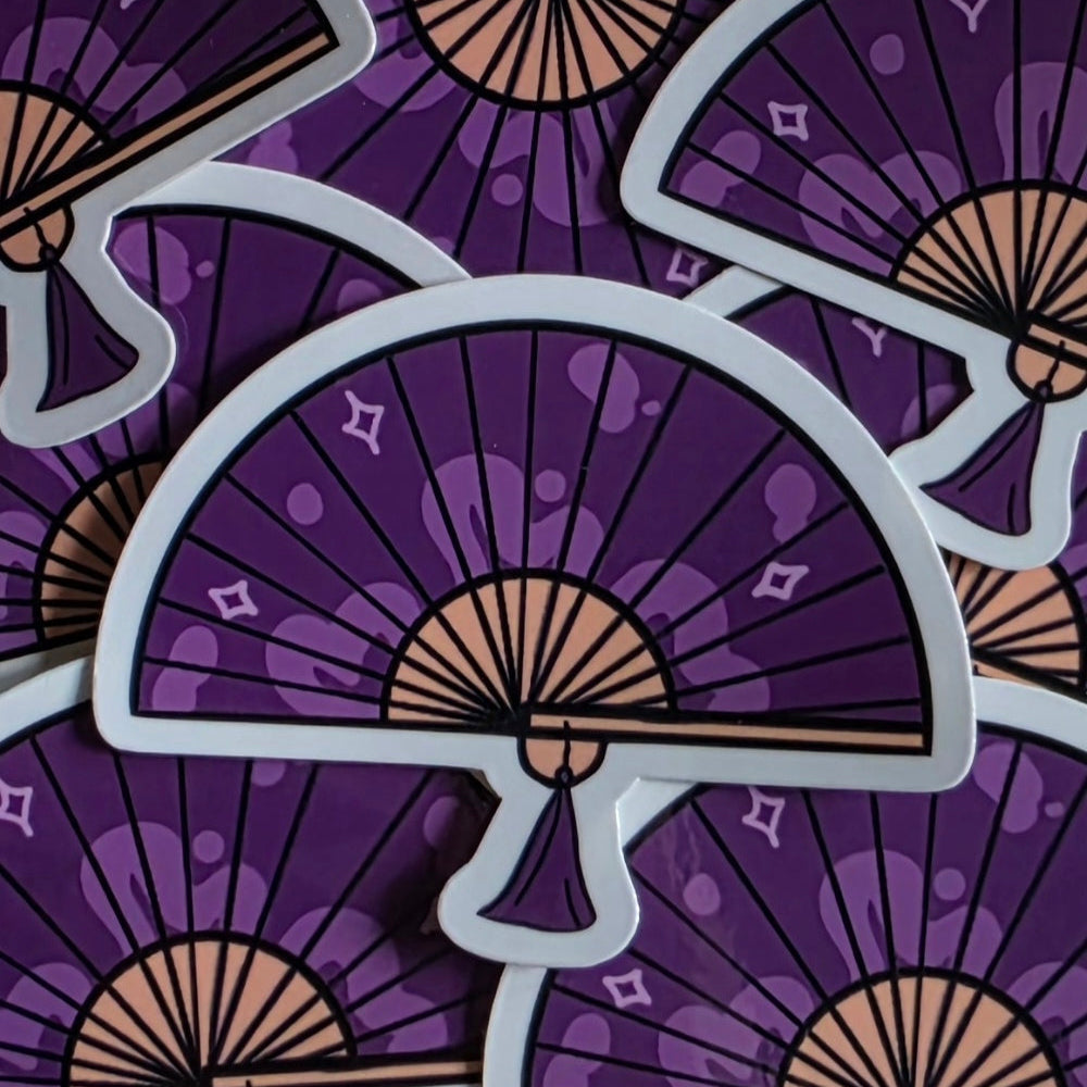 A close-up of several overlapping die-cut stickers featuring a purple hand fan design with beige ribs and light gray outlines, set against a matching patterned purple background.