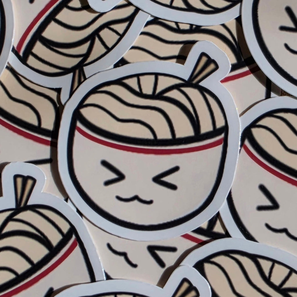 A close-up of multiple die-cut stickers featuring a cartoon ramen bowl character with a winking, cute face. The stickers are arranged overlapping.