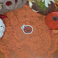 A sticker in the shape of a roast turkey sitting on an orange doily with autumn decor in the background.