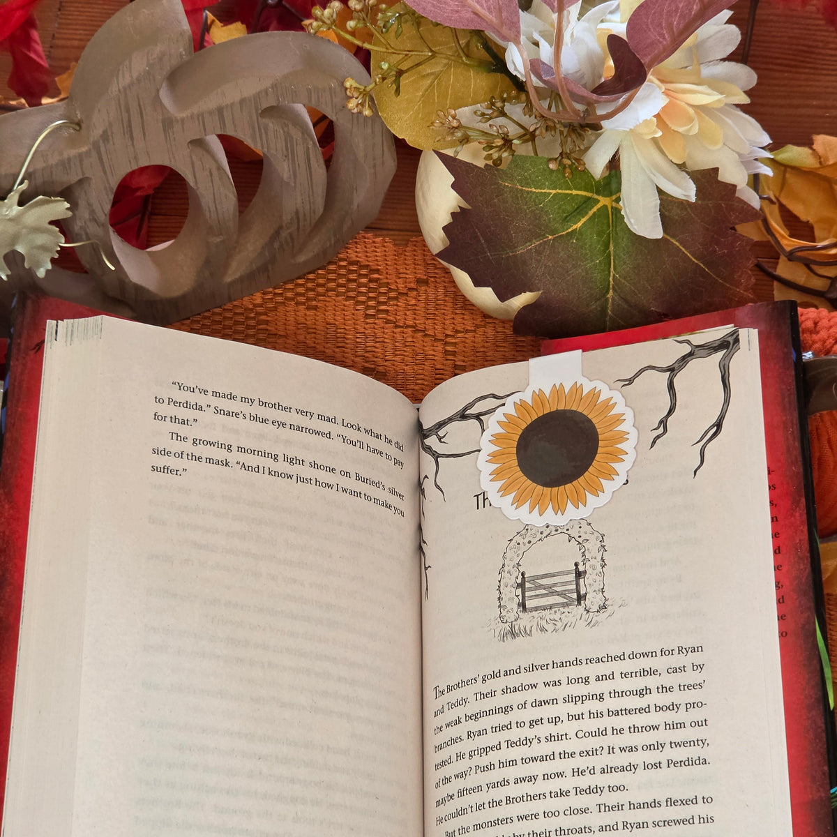 Sunflower magnetic bookmark clasped on a page of a book with autumn decorations in the background.