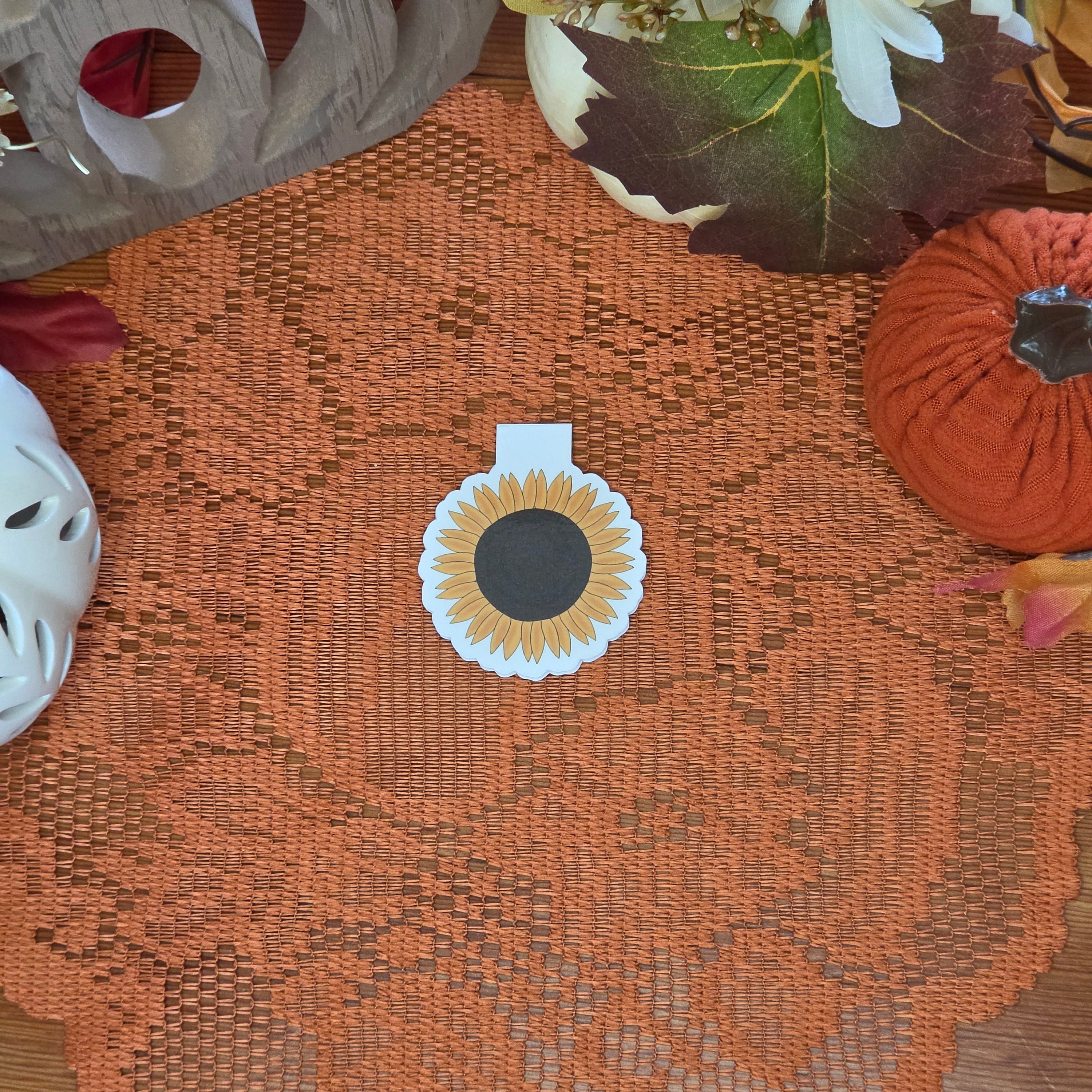 Sunflower magnetic bookmark set on orange doily with autumn decorations in the background.