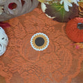 A sticker in the shape of a sunflower sitting on an orange doily with autumn decor in the background.