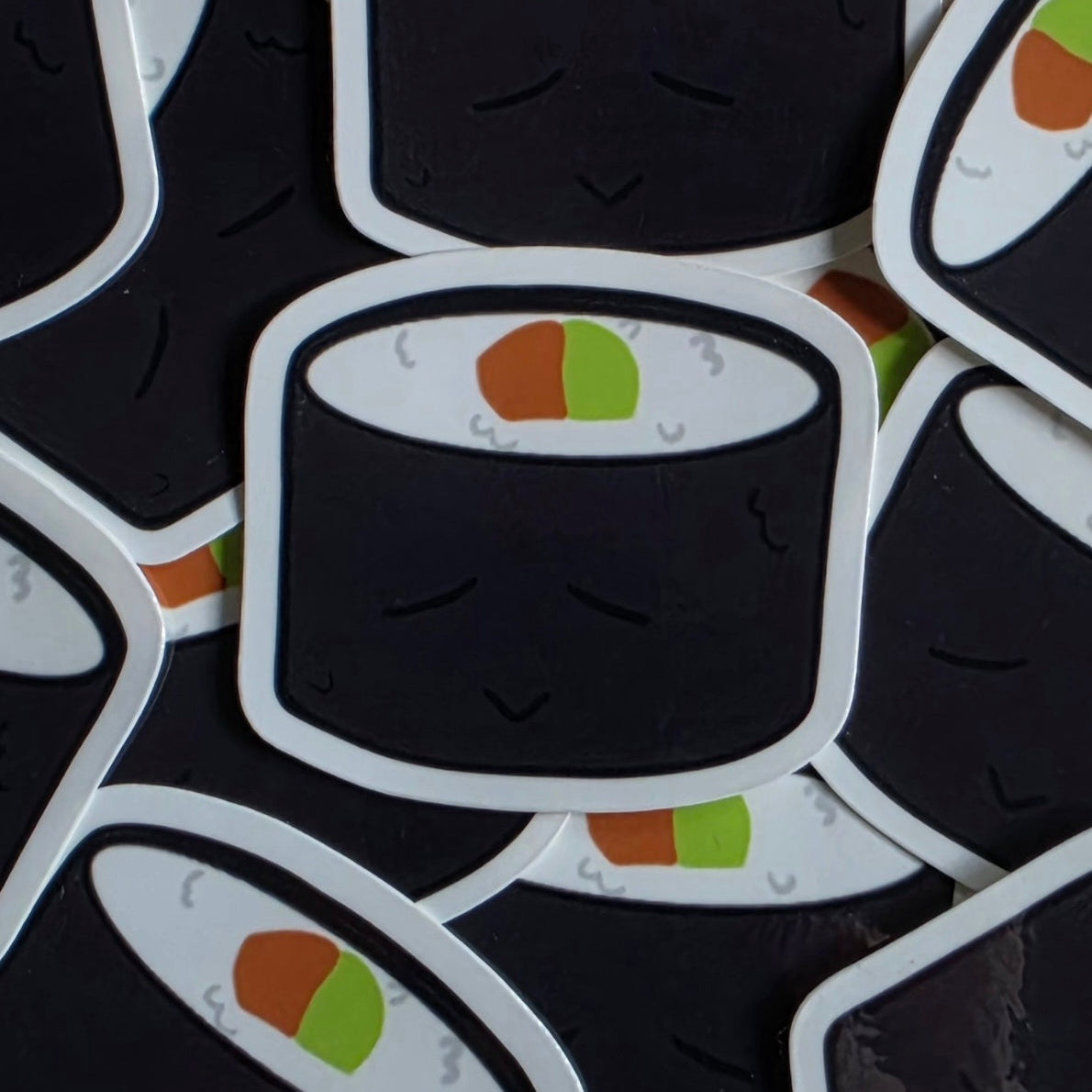A close-up of several die-cut stickers featuring cute cartoon sushi characters with closed eyes, arranged overlapping on a dark background.