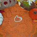 A sticker in the shape of a three pumpkins sticker sitting on an orange doily with autumn decor in the background.