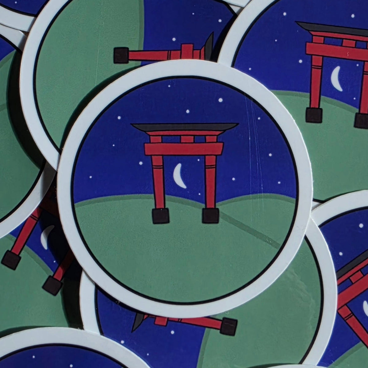 A close-up of round stickers featuring a red torii gate at night under a starry blue sky with a crescent moon, surrounded by a white border.